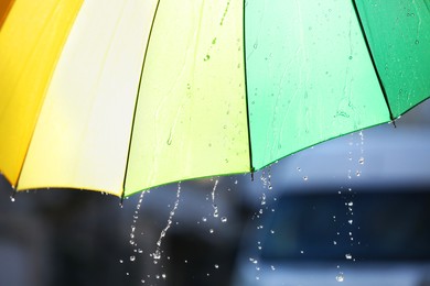 Photo of Open bright umbrella under pouring rain outdoors, closeup