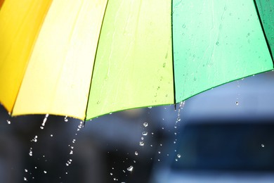 Photo of Open bright umbrella under pouring rain outdoors, closeup