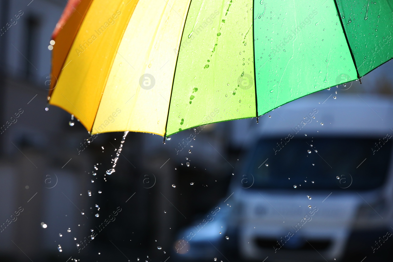 Photo of Open bright umbrella under pouring rain outdoors, closeup