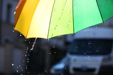 Photo of Open bright umbrella under pouring rain outdoors, closeup