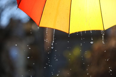 Photo of Open bright umbrella under pouring rain outdoors, closeup