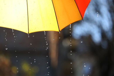 Photo of Open bright umbrella under pouring rain outdoors, closeup