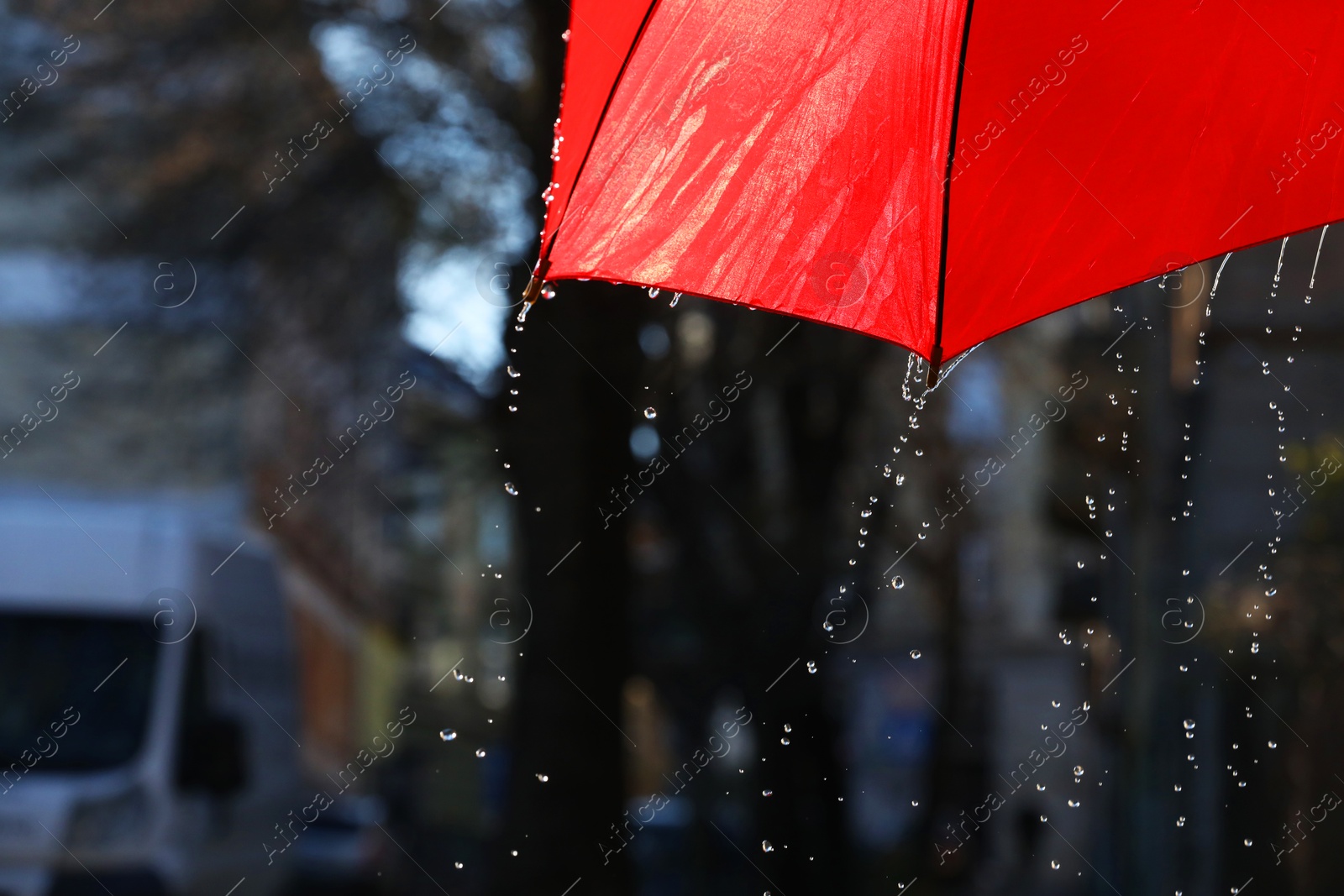 Photo of Open red umbrella under pouring rain outdoors, closeup