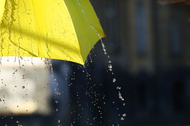 Photo of Open yellow umbrella under pouring rain outdoors, closeup. Space for text