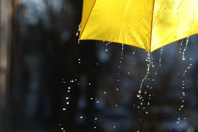 Photo of Open yellow umbrella under pouring rain outdoors, closeup