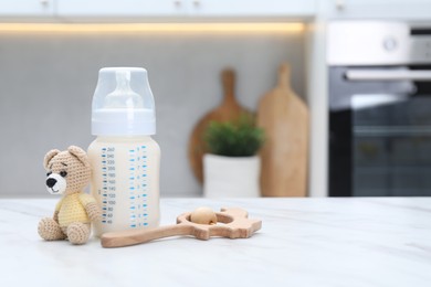 Photo of Feeding bottle with milk and toys on white table indoors. Space for text