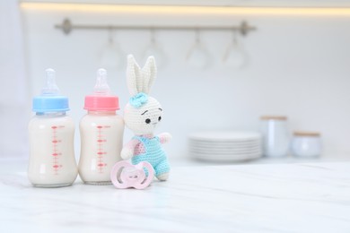 Photo of Feeding bottles with baby formula, pacifier and toy bunny on white table indoors. Space for text