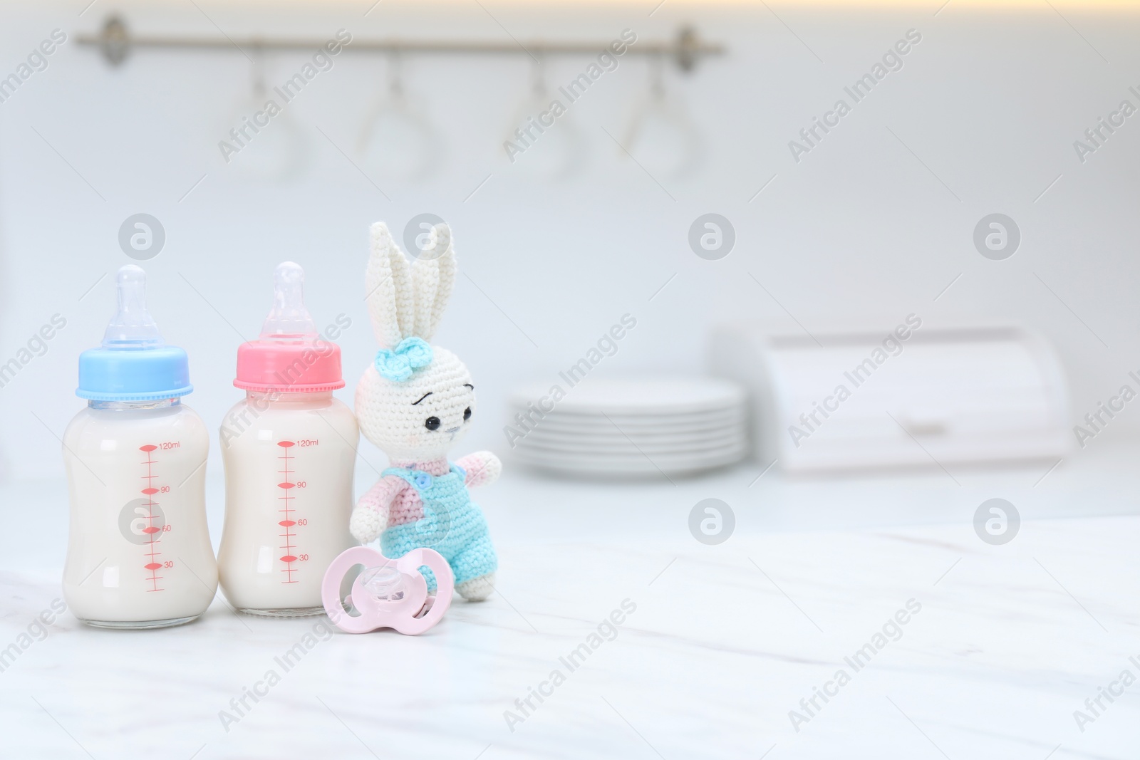 Photo of Feeding bottles with baby formula, pacifier and toy bunny on white table indoors. Space for text