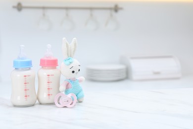 Photo of Feeding bottles with baby formula, pacifier and toy bunny on white table indoors. Space for text