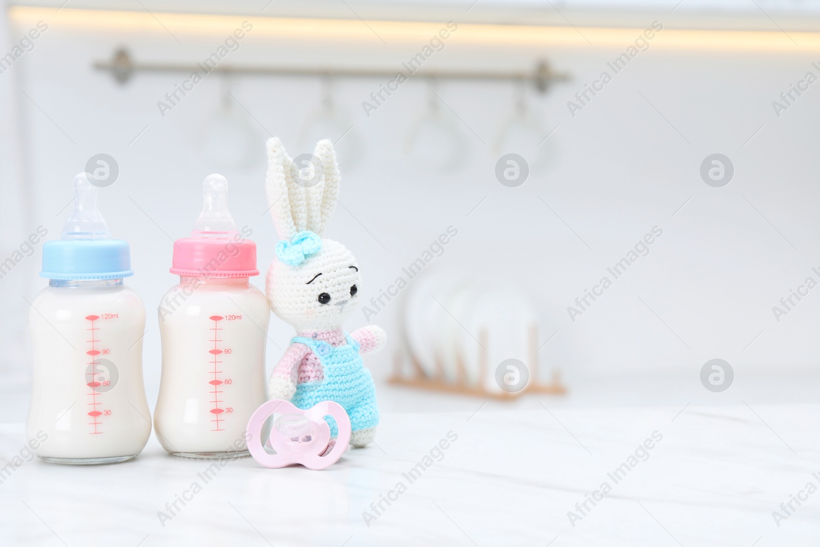 Photo of Feeding bottles with baby formula, pacifier and toy bunny on white table indoors. Space for text