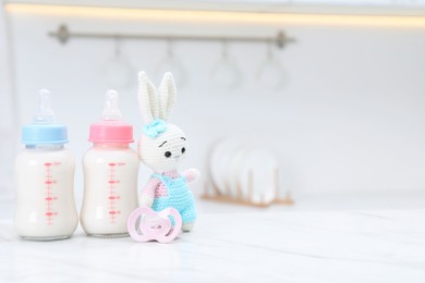 Photo of Feeding bottles with baby formula, pacifier and toy bunny on white table indoors. Space for text