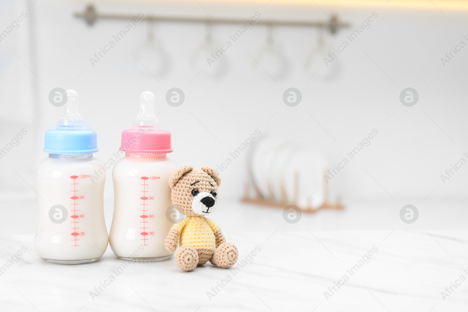 Photo of Feeding bottles with baby formula and teddy bear on white table indoors. Space for text