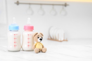 Photo of Feeding bottles with baby formula and teddy bear on white table indoors. Space for text