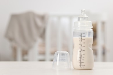 Photo of Feeding bottle with milk on white table indoors. Space for text