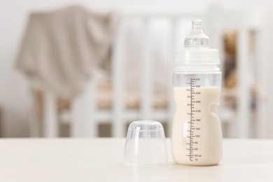 Photo of Feeding bottle with milk on white table indoors. Space for text