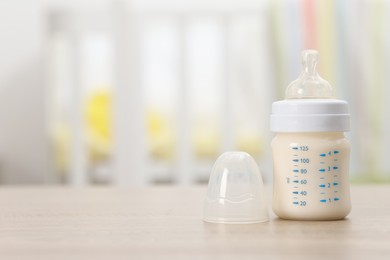 Photo of Feeding bottle with baby formula on wooden table indoors. Space for text