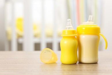 Photo of Feeding bottles with milk on wooden table indoors