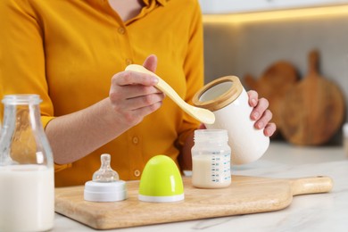 Photo of Mother making baby formula in feeding bottle at table indoors, closeup