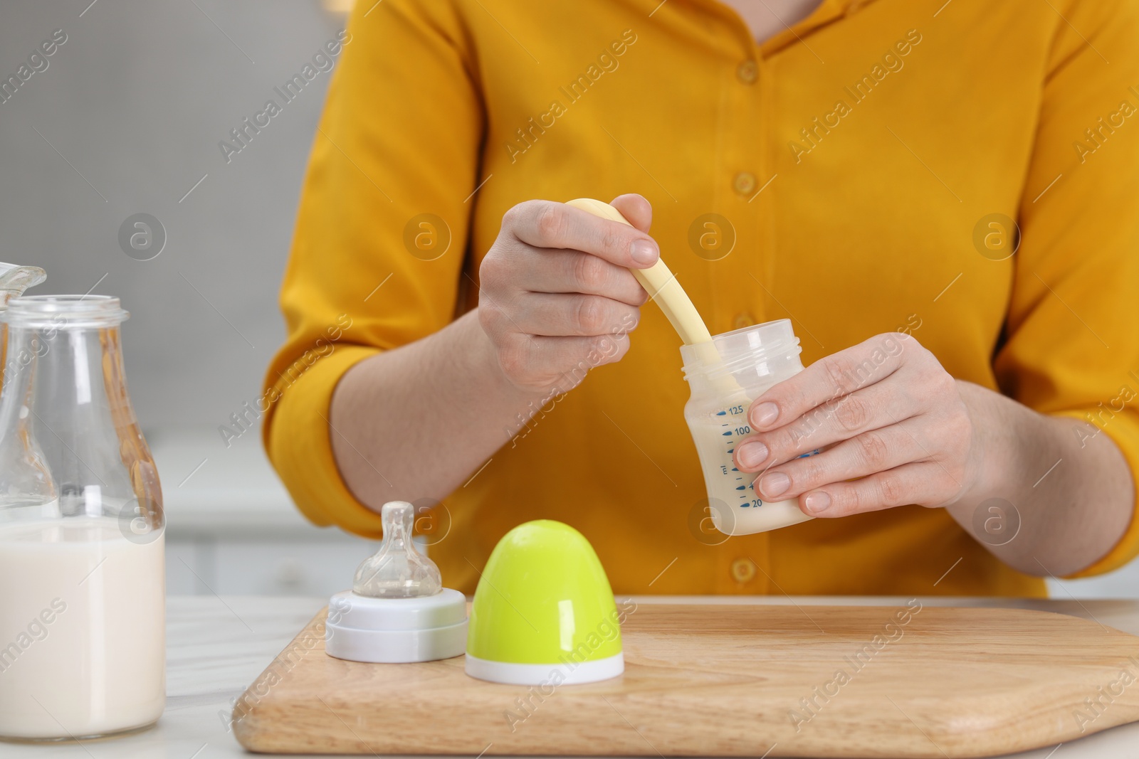 Photo of Mother making baby formula in feeding bottle at table indoors, closeup