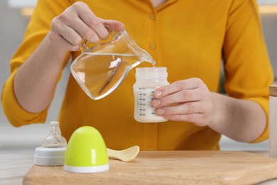 Photo of Mother making baby formula in feeding bottle at table indoors, closeup