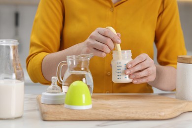 Photo of Mother making baby formula in feeding bottle at table indoors, closeup