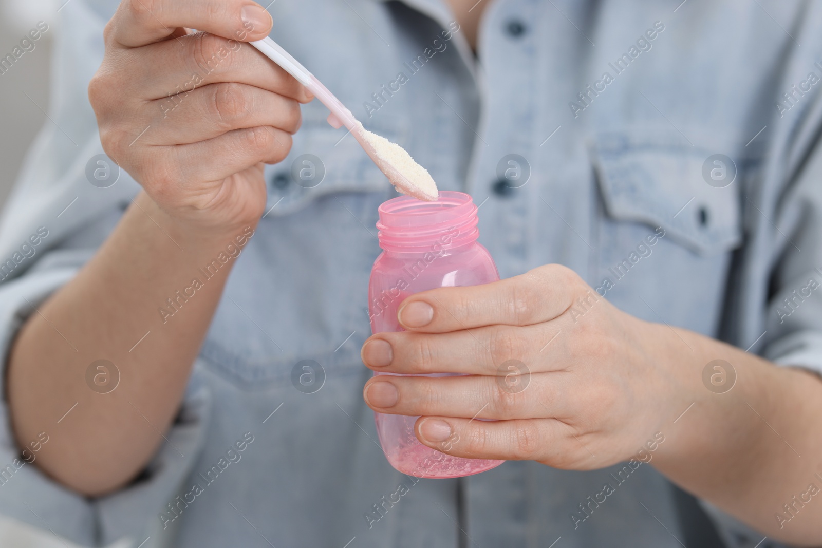 Photo of Mother making baby formula in feeding bottle indoors, closeup