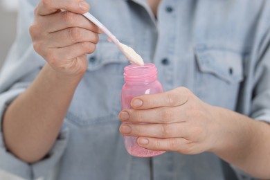 Photo of Mother making baby formula in feeding bottle indoors, closeup