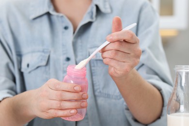 Photo of Mother making baby formula in feeding bottle indoors, closeup