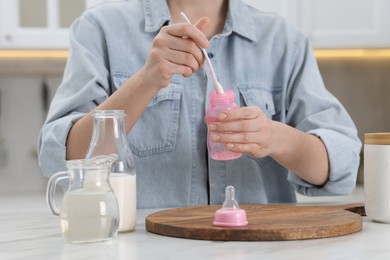 Photo of Mother making baby formula in feeding bottle at table indoors, closeup