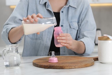 Photo of Mother making baby formula in feeding bottle at table indoors, closeup