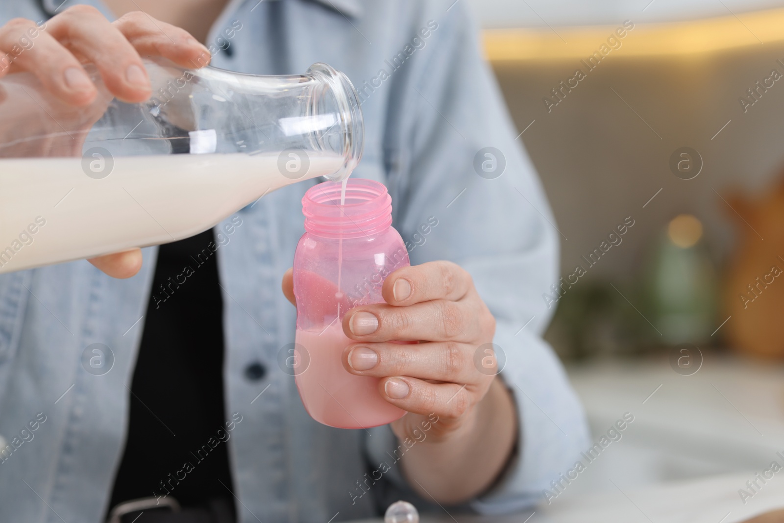 Photo of Mother making baby formula in feeding bottle indoors, closeup