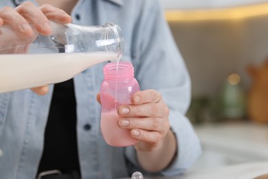 Photo of Mother making baby formula in feeding bottle indoors, closeup