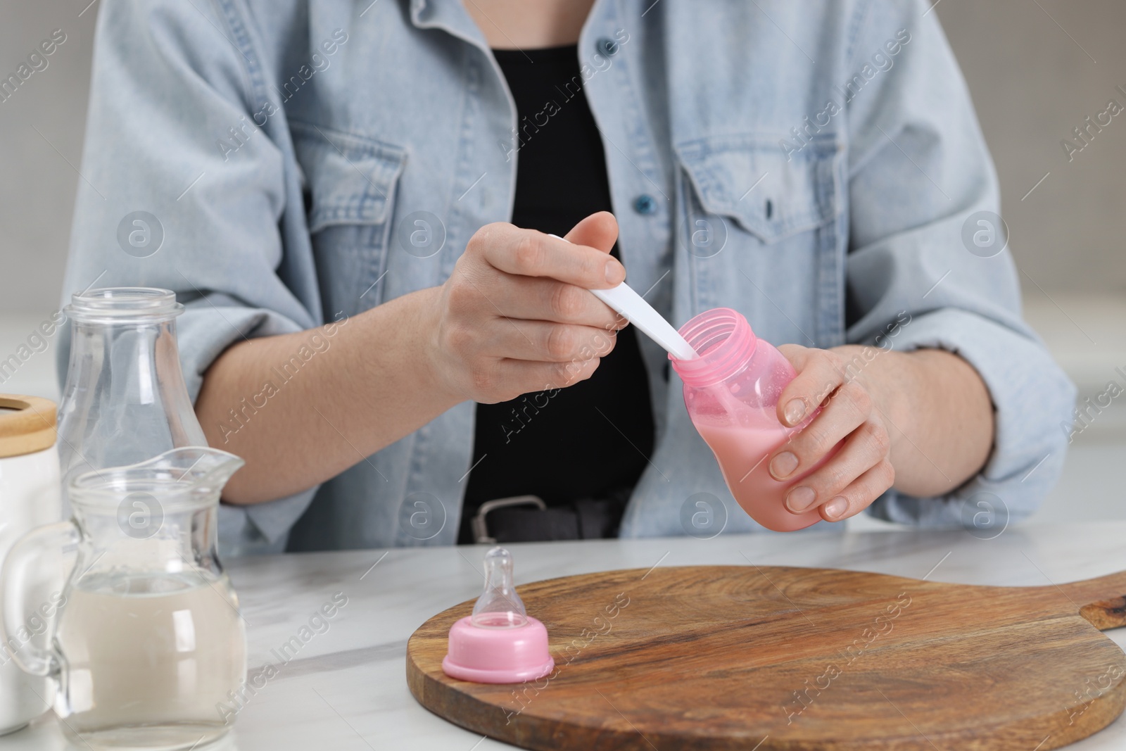 Photo of Mother making baby formula in feeding bottle at table indoors, closeup