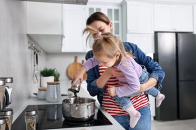 Photo of Busy housewife cooking with her little daughter in kitchen