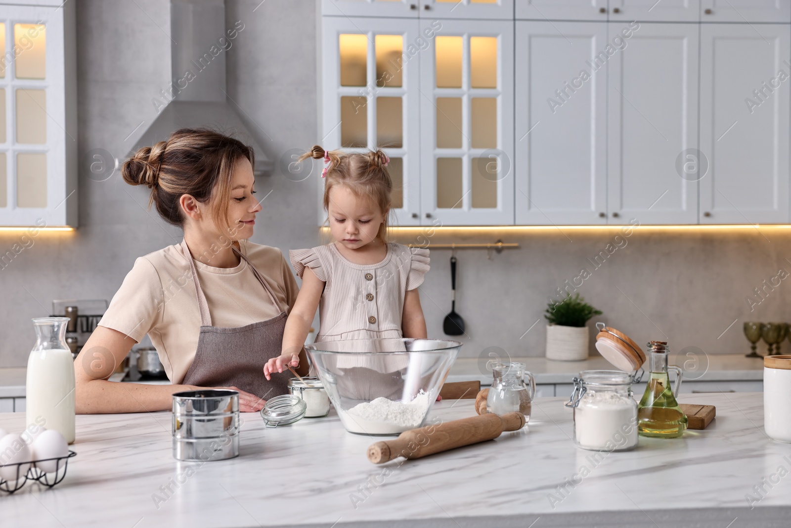 Photo of Housewife cooking with her little daughter at marble table in kitchen