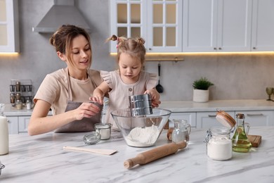 Photo of Smiling housewife cooking with her little daughter at marble table in kitchen