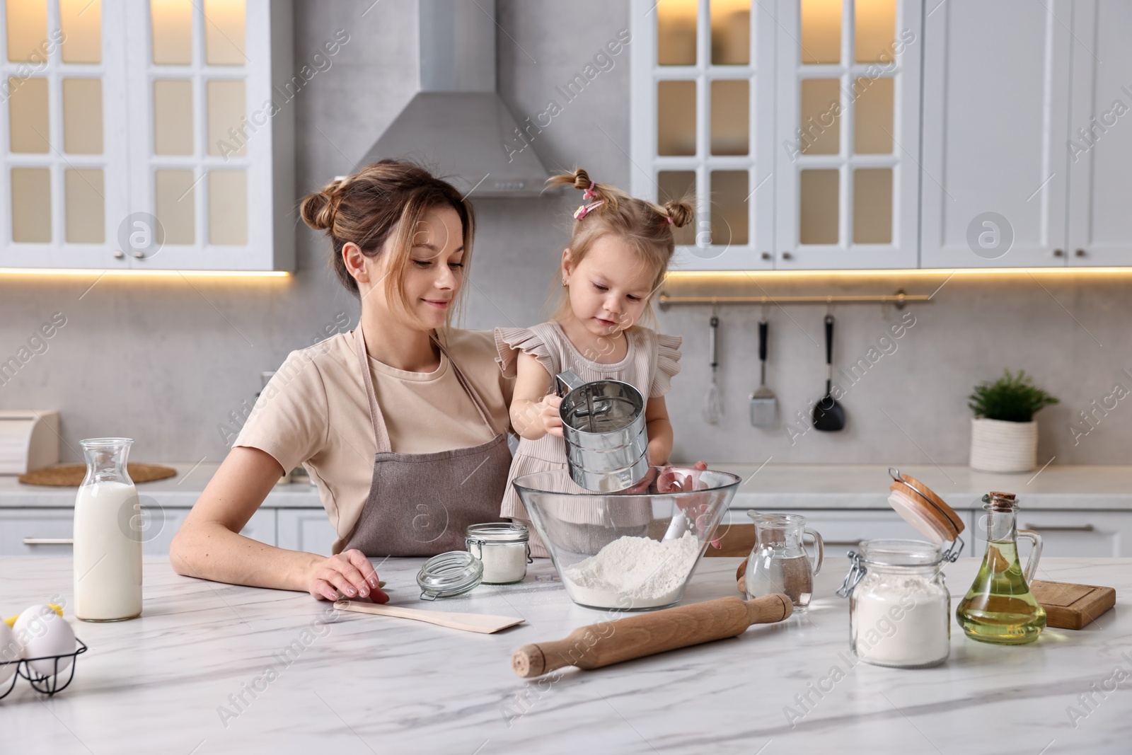 Photo of Housewife cooking with her little daughter at marble table in kitchen