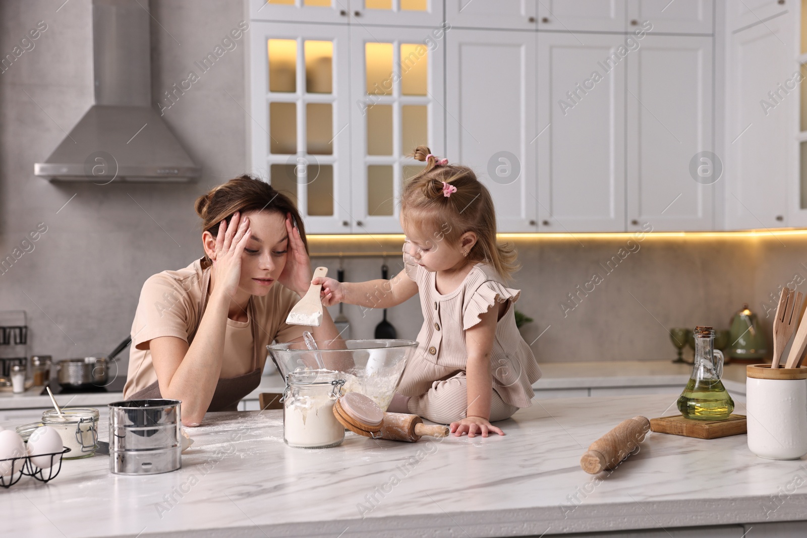 Photo of Tired housewife cooking with her little daughter at marble countertop in kitchen