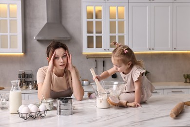 Photo of Tired housewife cooking with her little daughter at marble table in kitchen