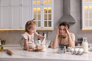 Photo of Tired housewife cooking with her little daughter at marble table in kitchen