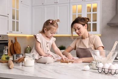 Photo of Smiling housewife cooking with her little daughter at marble table in kitchen