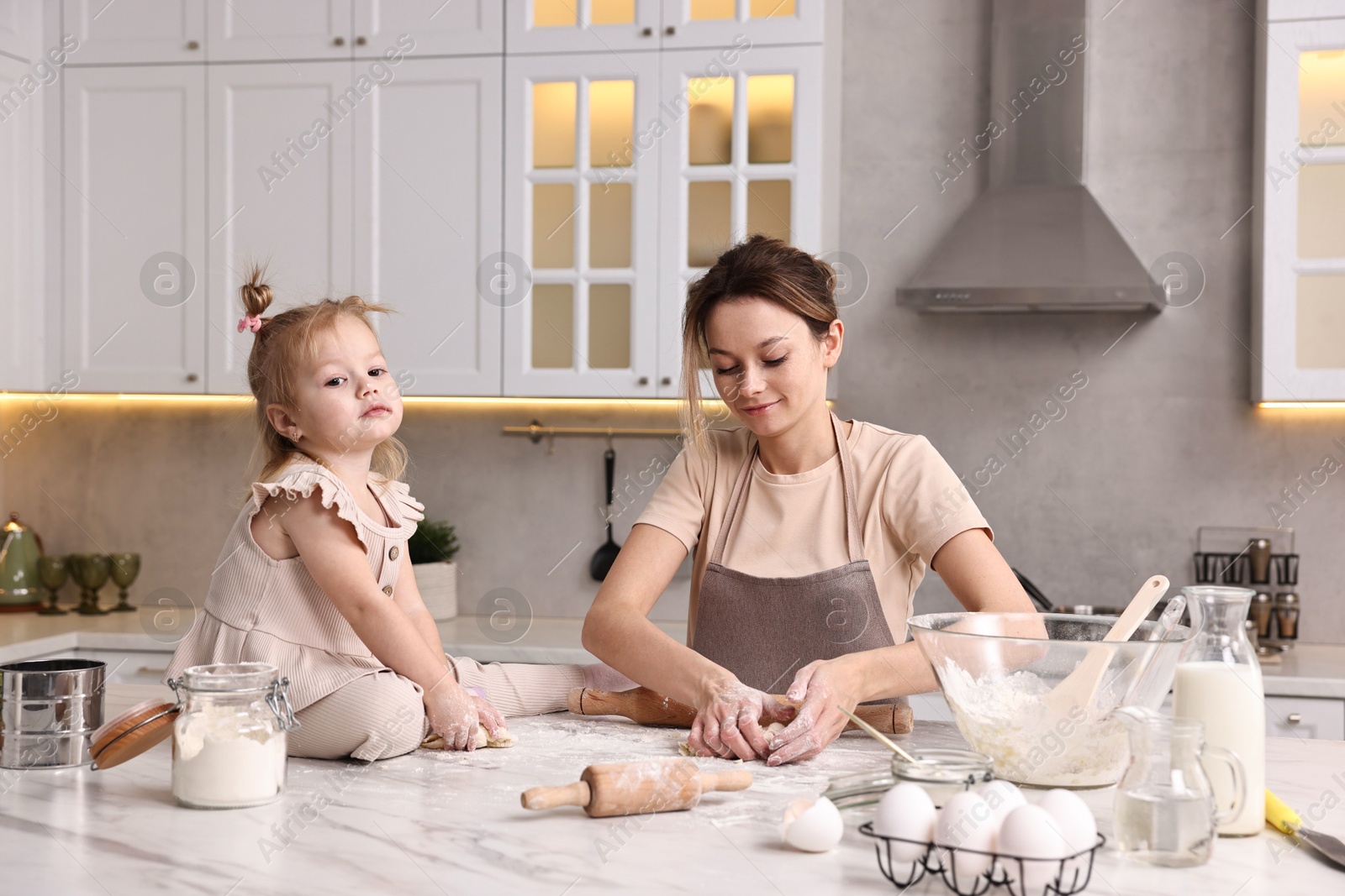 Photo of Housewife cooking with her little daughter at marble table in kitchen