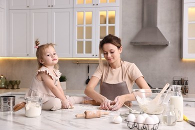 Photo of Housewife cooking with her little daughter at marble table in kitchen