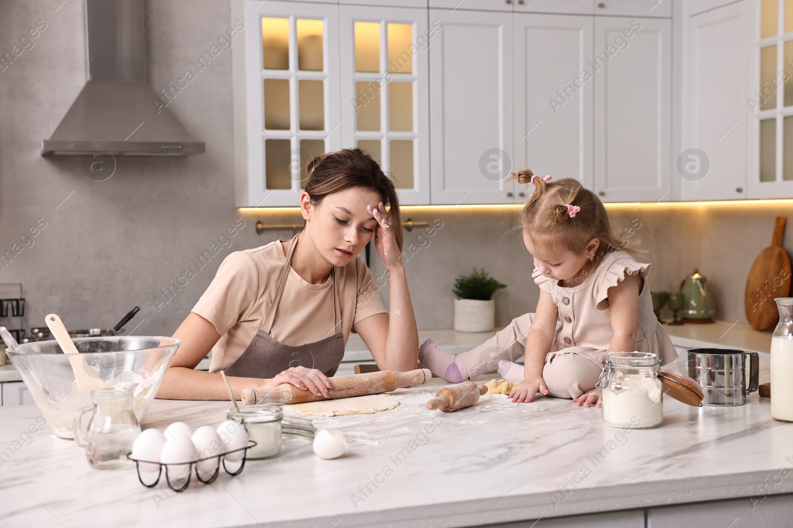 Photo of Tired housewife cooking with her little daughter at marble table in kitchen