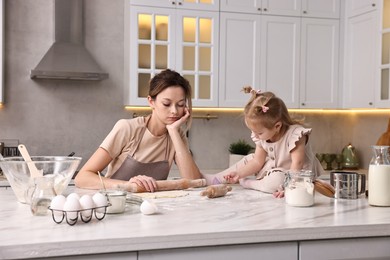 Photo of Tired housewife cooking with her little daughter at marble countertop in kitchen