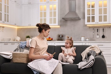 Photo of Housewife with her little daughter among messy laundry on sofa at home