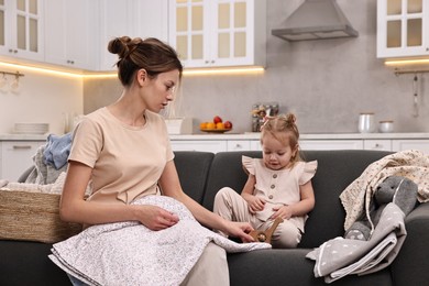 Photo of Housewife with her little daughter among messy laundry on sofa at home