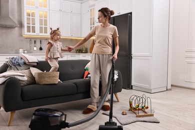 Housewife talking with her little daughter while cleaning floor with vacuum cleaner at home