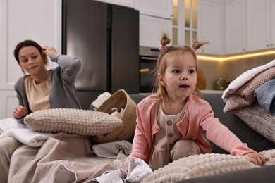 Photo of Housewife with her little daughter among messy laundry on sofa at home, selective focus