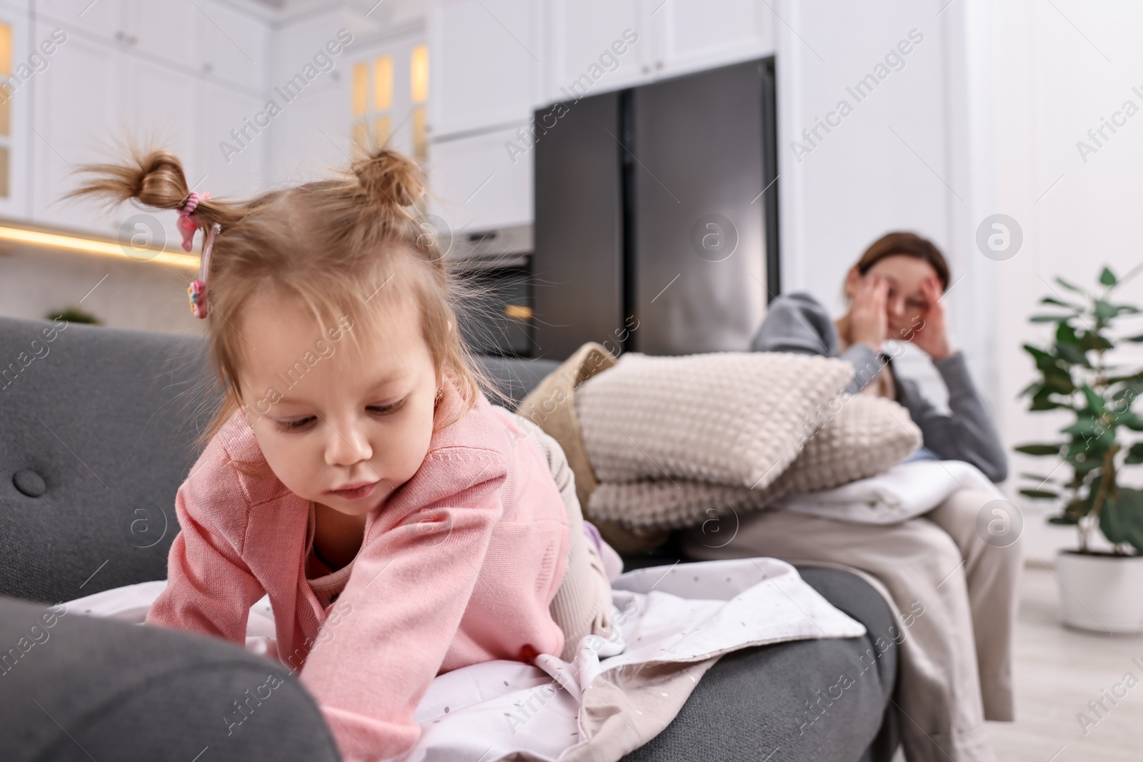 Photo of Tired housewife with her little daughter among messy laundry on sofa at home, selective focus